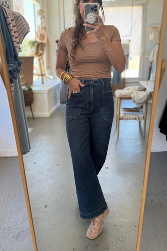 Person wearing a brown top and blue jeans standing in front of a mirror.