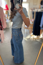 Load image into Gallery viewer, Person wearing a light blue t-shirt and high-waisted jeans in a clothing store.