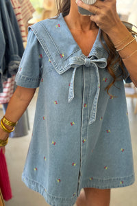 Woman wearing a denim dress with a bow detail, taking a mirror selfie.