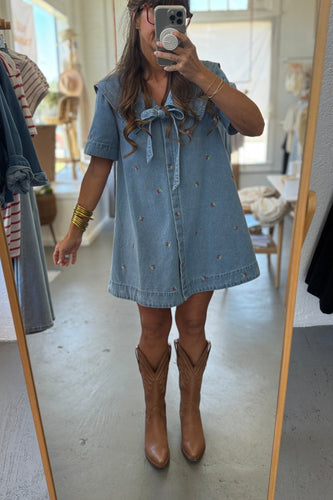 Person wearing a denim dress with a bow and brown boots in a room.