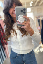 Load image into Gallery viewer, Woman taking a mirror selfie wearing a white sweater and blue jeans in a store setting.