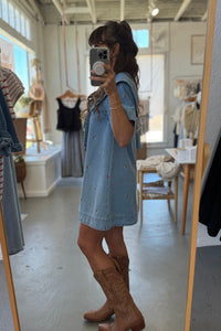 Person wearing a denim dress and brown boots in a clothing store.