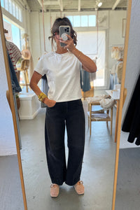 Person taking a mirror selfie wearing a white t-shirt and black pants in a store.