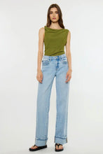 Load image into Gallery viewer, A model wearing a sleeveless olive green top and light-wash wide-leg blue jeans, standing against a plain white studio background.