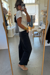 Person taking a mirror selfie wearing a white t-shirt and black pants in a room with a large mirror.