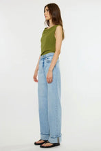 Load image into Gallery viewer, A woman modeling a sleeveless olive green top and light-wash wide-leg blue jeans against a plain white studio background.