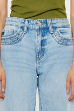Load image into Gallery viewer, Close-up of a person wearing light-wash blue denim jeans with a green top visible at the waist.