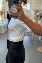 Load image into Gallery viewer, Person taking a mirror selfie wearing a white t-shirt and black pants in an indoor setting.