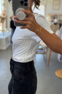 Person taking a mirror selfie wearing a white t-shirt and black pants in an indoor setting.