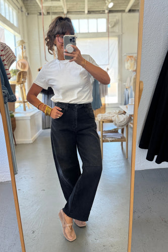 Person taking a mirror selfie wearing a white top and black pants in a room with a mirror and clothing.