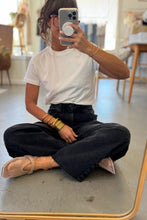 Load image into Gallery viewer, Person sitting on a mirror taking a selfie wearing a white shirt and black pants.