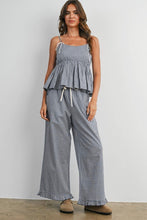 Load image into Gallery viewer, A woman modeling a matching two-piece gingham set consisting of a sleeveless peplum top with tie straps and wide-leg pants, in a black and white checkered pattern, standing against a plain light gray wall.