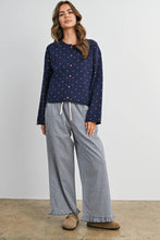 Load image into Gallery viewer, A woman modeling a two-piece pajama set consisting of a navy blue long-sleeve top with small pink and white polka dots, and matching wide-leg pants in a small-scale blue and white gingham pattern. She is wearing brown suede slippers against a neutral studio backdrop.