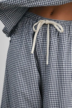 Load image into Gallery viewer, Close-up of a person wearing loose gingham pajama pants with a white drawstring at the waist, cropped to show the torso and upper legs.
