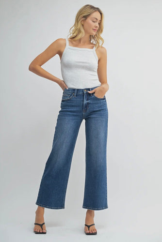 Woman wearing a white tank top and blue jeans on a plain background