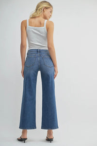 Woman wearing blue jeans and a white tank top on a plain background