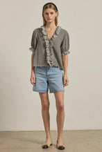 Load image into Gallery viewer, Woman wearing a checkered blouse with ruffled details and denim shorts against a neutral background