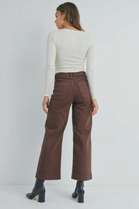 Person wearing brown pants and a white top on a plain background