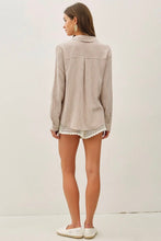 Load image into Gallery viewer, A woman shown from the back wearing a light beige long-sleeve button-up shirt with a pleated back and white shorts, standing against a plain off-white wall.