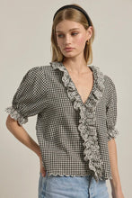 Load image into Gallery viewer, Woman wearing a black and white checkered blouse with ruffled details on a beige background