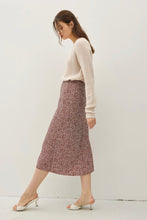 Load image into Gallery viewer, A woman wearing a cream knit long-sleeve top and a pinkish-red patterned midi skirt, paired with white heeled mule sandals, standing against a plain off-white wall.