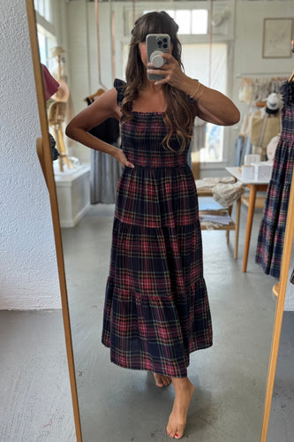 Woman taking a mirror selfie wearing a plaid dress in a room.