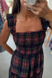 Woman wearing a plaid dress taking a mirror selfie.