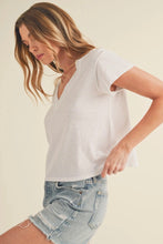 Load image into Gallery viewer, A woman wearing a white short-sleeve V-neck t-shirt and light-wash distressed denim shorts, photographed against a solid light beige background.