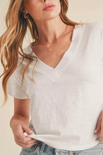 Load image into Gallery viewer, A woman wearing a white short-sleeve V-neck t-shirt and light-wash blue jeans, shown from the chest up against a warm beige background.