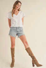 Load image into Gallery viewer, A woman modeling a white short-sleeve V-neck t-shirt, light-wash denim shorts with raw hems, and brown knee-high suede boots against a solid beige studio background.
