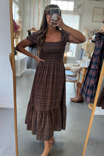 Woman taking a mirror selfie wearing a brown plaid dress in a store.