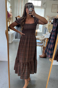 Woman taking a mirror selfie wearing a brown plaid dress in a store.
