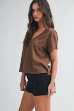 Load image into Gallery viewer, A woman modeling a brown short-sleeve V-neck top with black denim shorts against a light gray studio background.