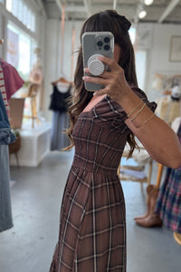 Person taking a mirror selfie wearing a plaid dress in a clothing store.