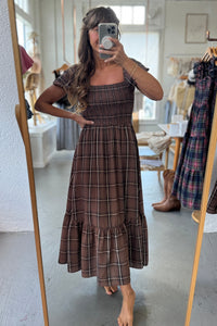 Woman wearing a brown plaid dress in a clothing store.