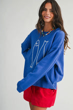 Load image into Gallery viewer, A woman wearing a bright blue knit sweater with a white fish line-art graphic on the front, paired with red shorts, against a plain light gray studio background.