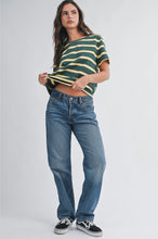 Load image into Gallery viewer, A woman modeling a green and yellow striped short-sleeve crop top with blue jeans and black sneakers, standing against a light gray studio background.