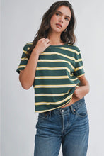 Load image into Gallery viewer, A woman modeling a short-sleeve crewneck t-shirt with horizontal dark green and mustard yellow stripes, paired with blue jeans, against a light gray studio background.