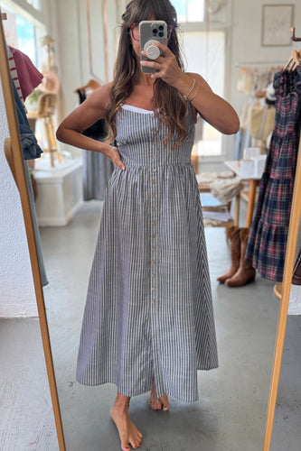 Woman taking a mirror selfie wearing a striped dress in a clothing store.