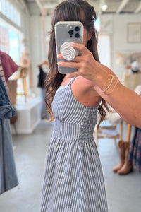 Person wearing a blue and white striped dress taking a mirror selfie in a store.