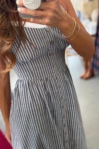 Person wearing a black and white striped dress with buttons, standing indoors.