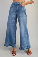 Load image into Gallery viewer, A person wearing high-waisted, wide-leg blue denim jeans with a ruffled hem and brown strappy sandals, shown from the waist down against a plain light gray studio background.