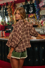 Load image into Gallery viewer, A woman in a brown and beige plaid button-up shirt and green velvet shorts with lace trim, standing in a bar setting.