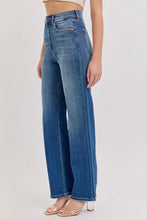 Load image into Gallery viewer, A model wearing a pair of high-waisted, wide-leg blue denim jeans with a faded wash, paired with clear high-heeled sandals, shown from the waist down against a plain light background.
