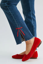 Load image into Gallery viewer, A close-up of a person's legs wearing blue jeans with a small red bow detail at the hem and bright red suede ballet flats with matching bows, set against a plain light gray background.