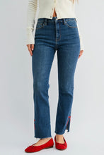 Load image into Gallery viewer, A model wearing a pair of high-waisted, straight-leg blue jeans with red embroidered details near the hem, styled with a cream cardigan and red flats against a light gray studio background.