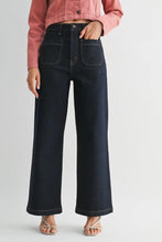 Load image into Gallery viewer, A model wearing dark wash wide-leg denim jeans, a pink cropped jacket, and beige strappy heels, shown from the waist down against a light gray studio background.