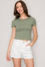 Load image into Gallery viewer, A woman modeling a cropped short-sleeve crewneck t-shirt in sage green, paired with white shorts, against a light gray studio background.
