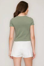Load image into Gallery viewer, A woman shown from the back wearing a short-sleeve cropped t-shirt in sage green and white shorts, standing against a plain light gray background.