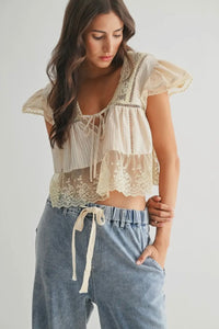 Woman wearing a lace top and blue pants against a plain background